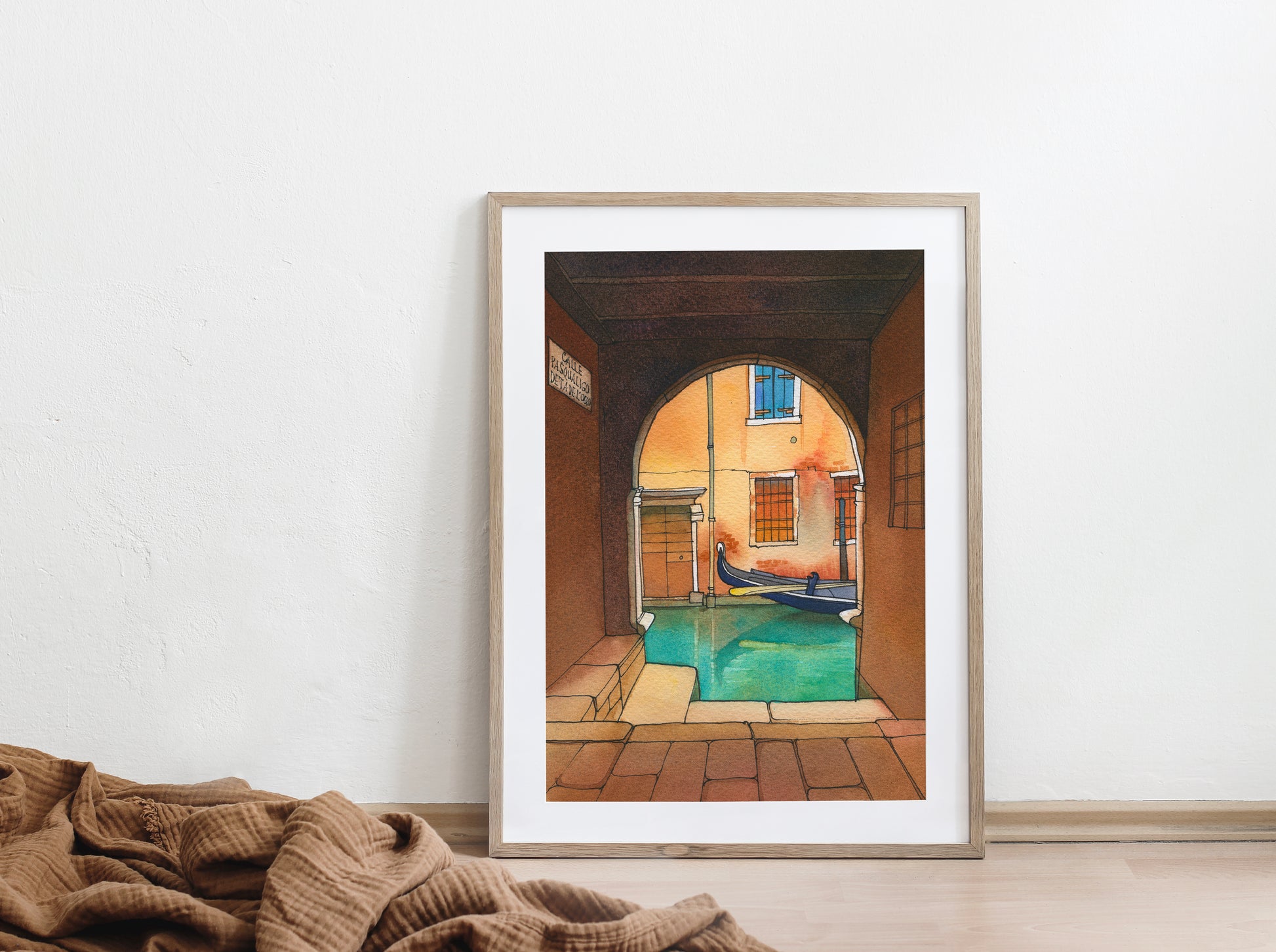 Framed watercolor and ink artwork of a venetian canal scene with an archway on a white wall.