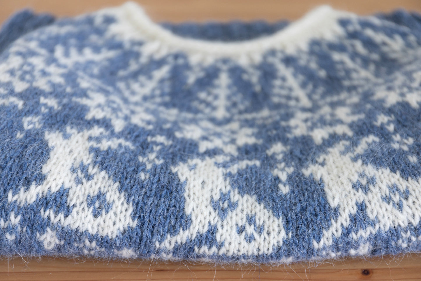 Close-up of a folded hand-knitted wool sweater with bunnies motif in bue and white