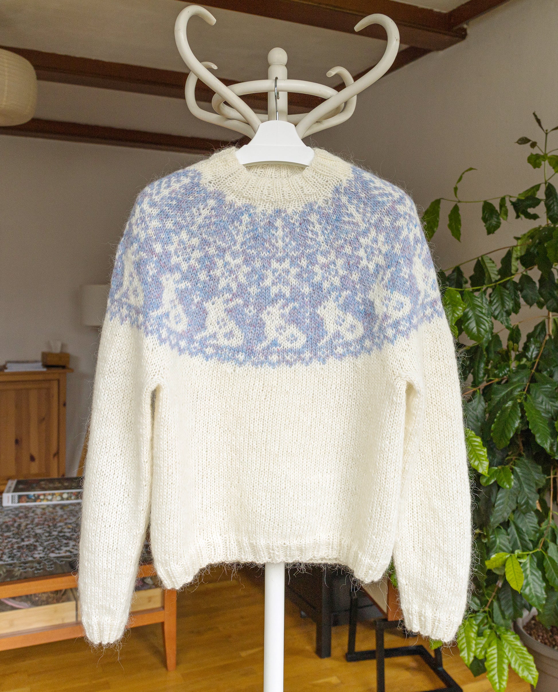 White and blue bunny yoke Vinterskog sweater on a hanger against a home interior background