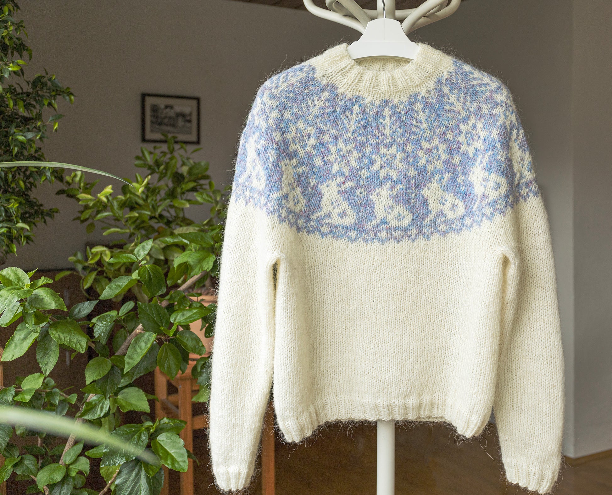 White lopapeysa sweater with bunnies motif yoke on a hanger against a neutral background