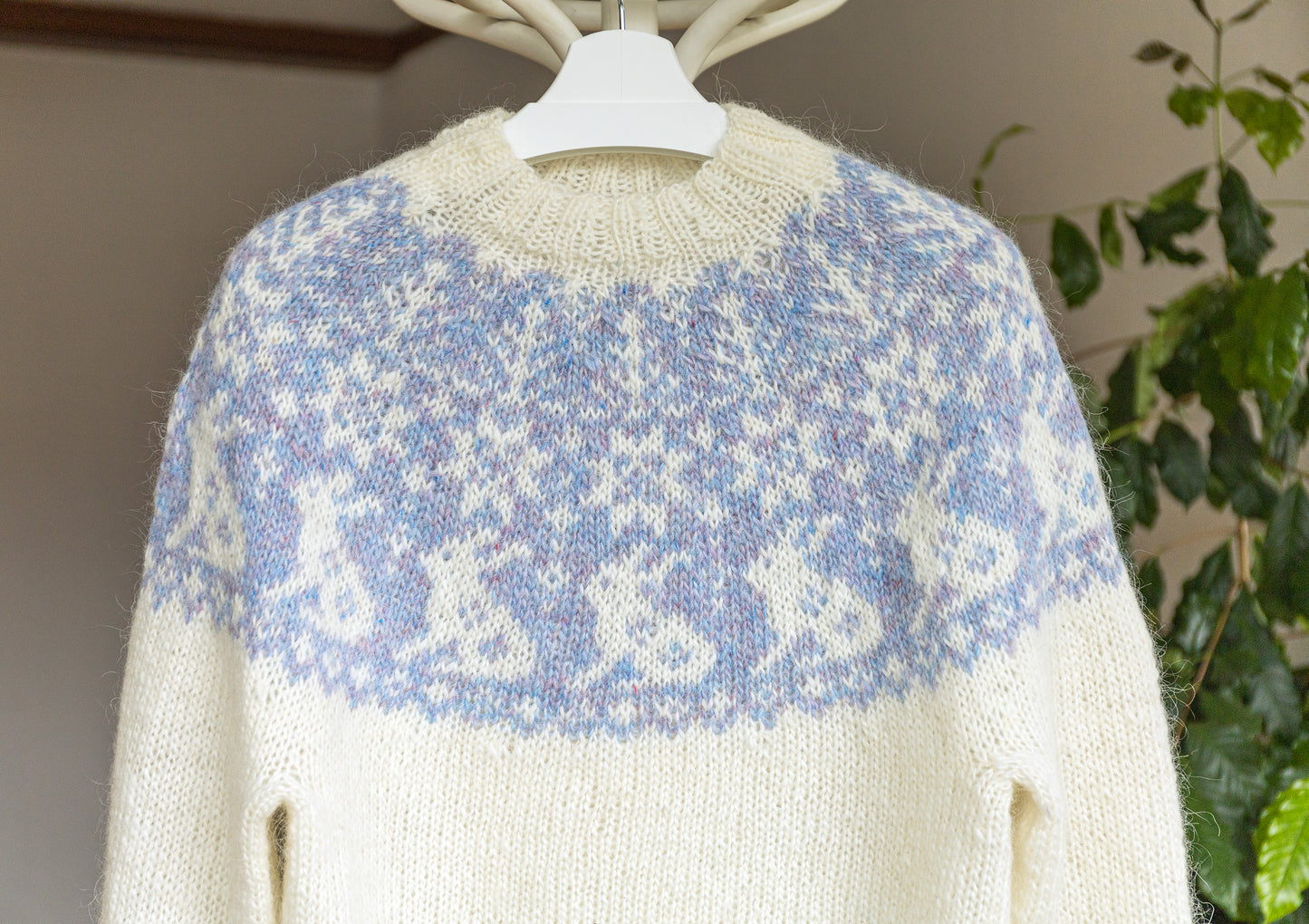 White sweater with blue bunny pattern on a hanger against a neutral background