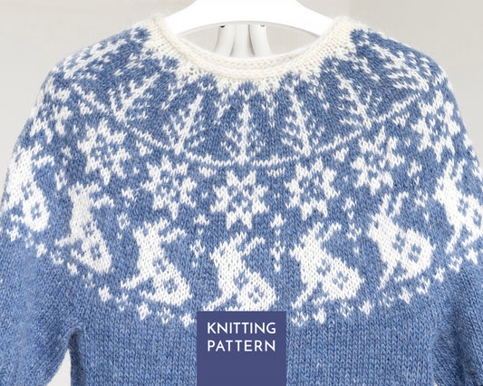 A close-up of a blue and white knitted sweater with a Fair Isle style bunny pattern, hanging on a white hanger against a light gray background