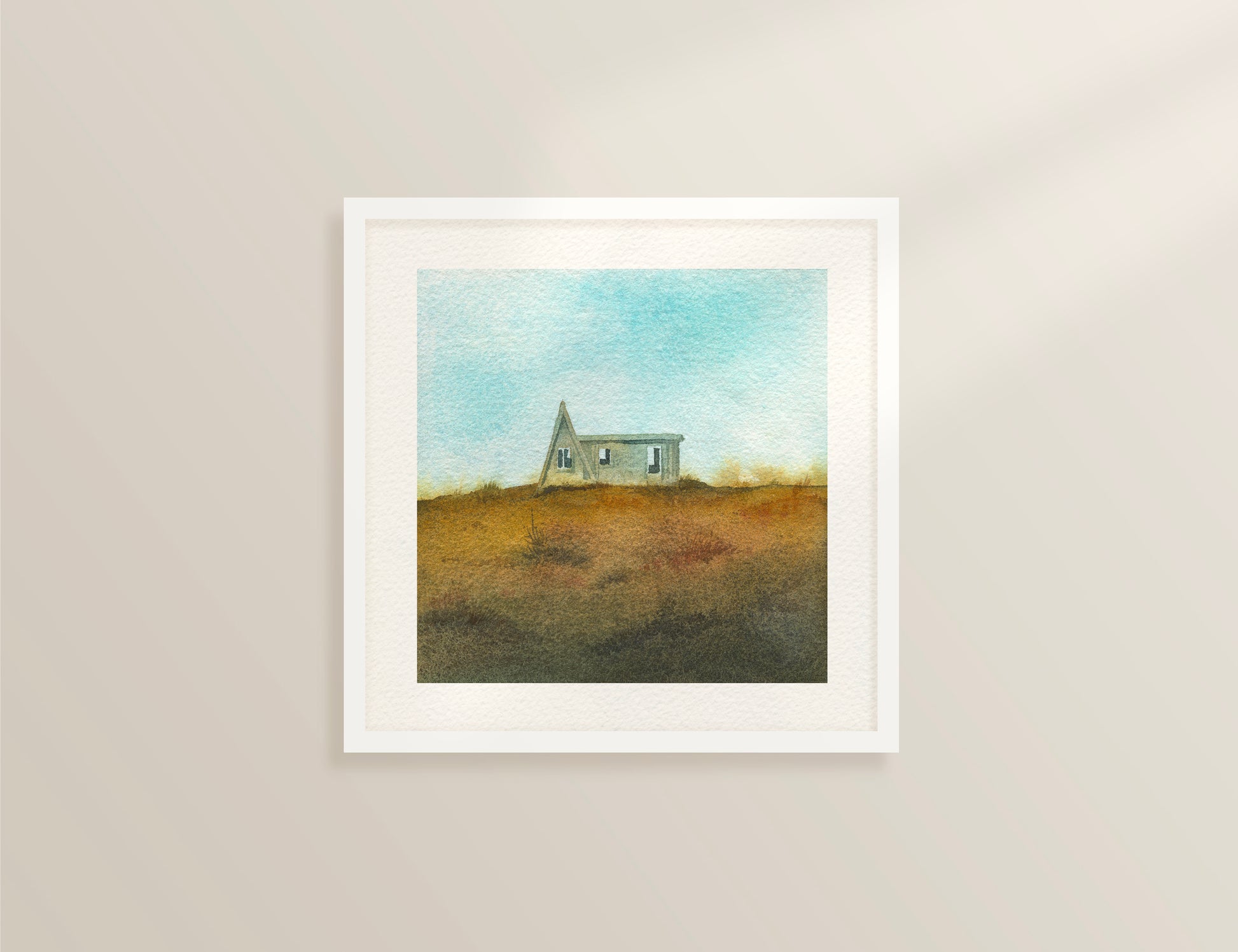 Framed watercolor painting featuring a small A-frame wooden cabin on a grassy hill under a light blue sky in the Westfjords, Iceland