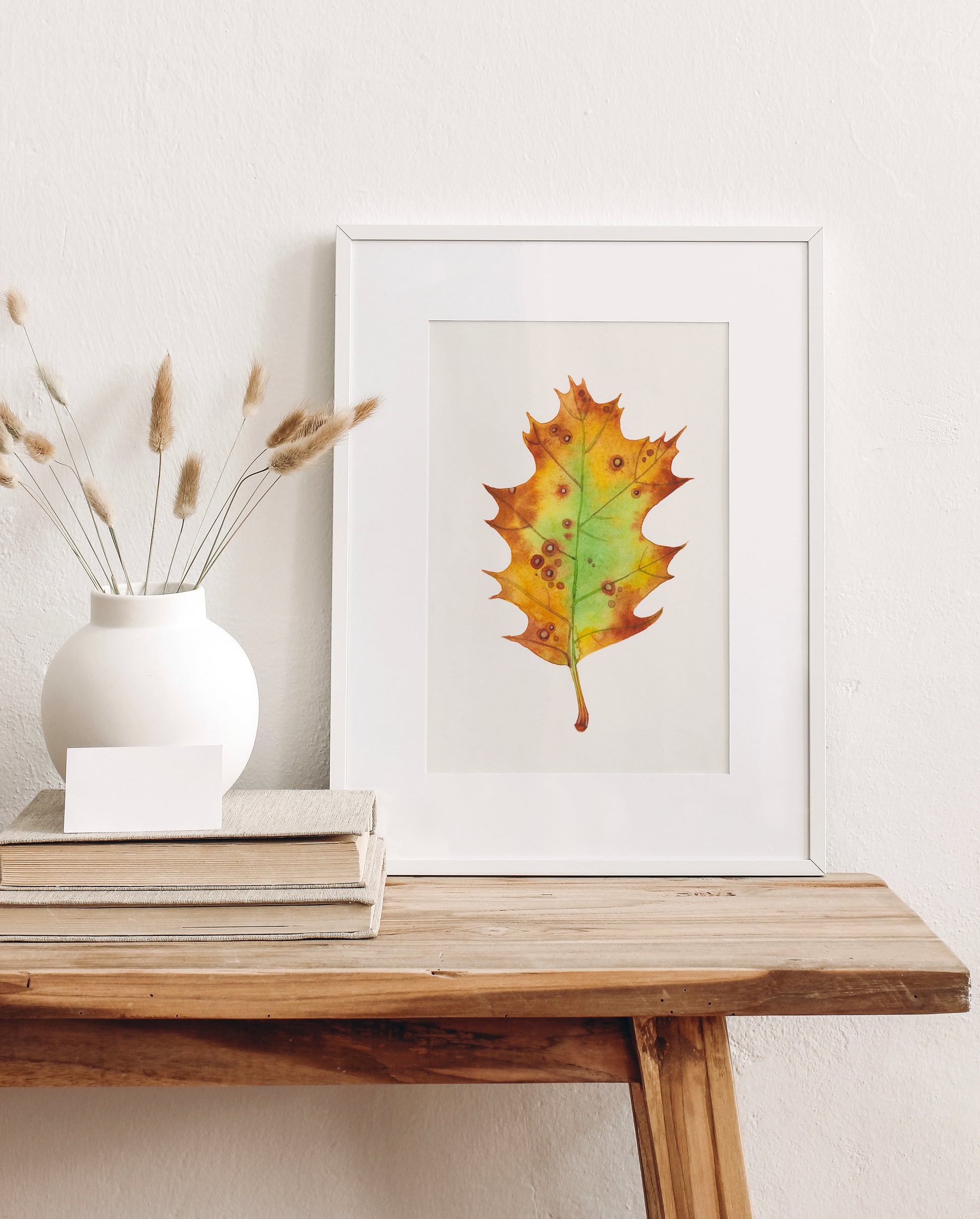 A framed watercolor painting of a dried oak leaf