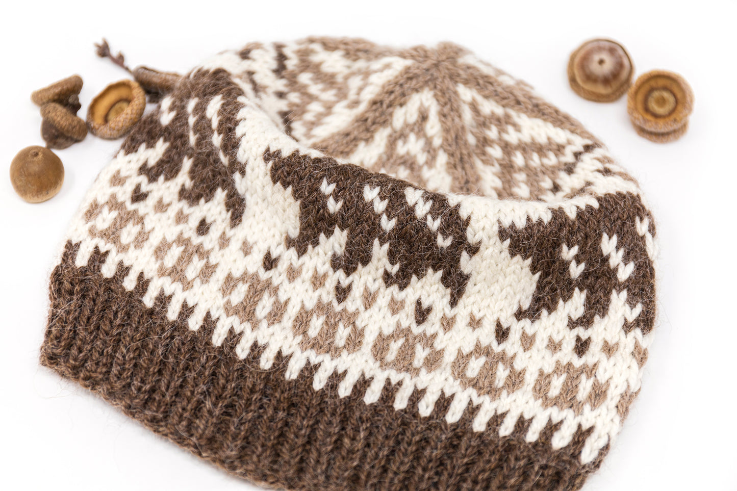 Knitted brown and white hat with bears motif and with acorns on a white background