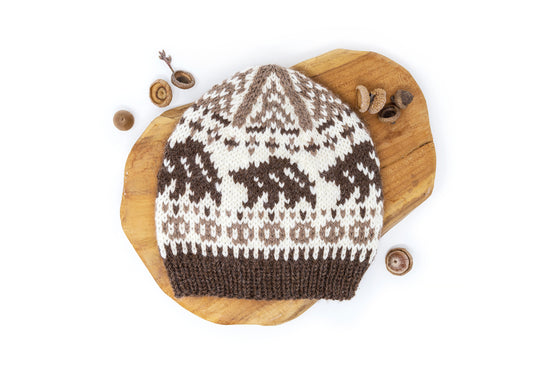 A hand-knitted wool alpaca hat with a bear pattern, displayed on a wooden surface.