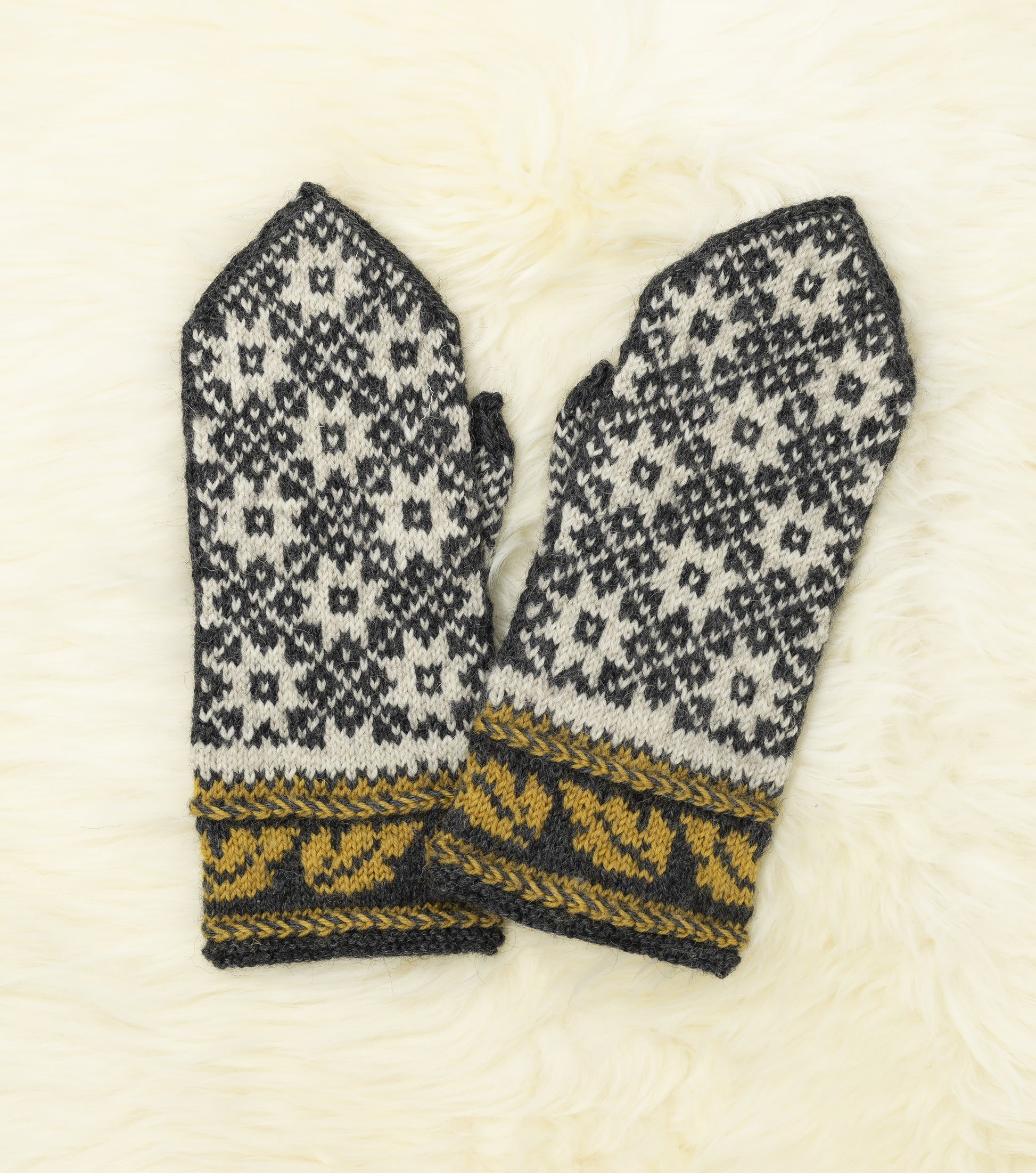 Front view of a pair of black, white and yellow hand-knitted mittens with traditional Estonian pattern on a white fur background