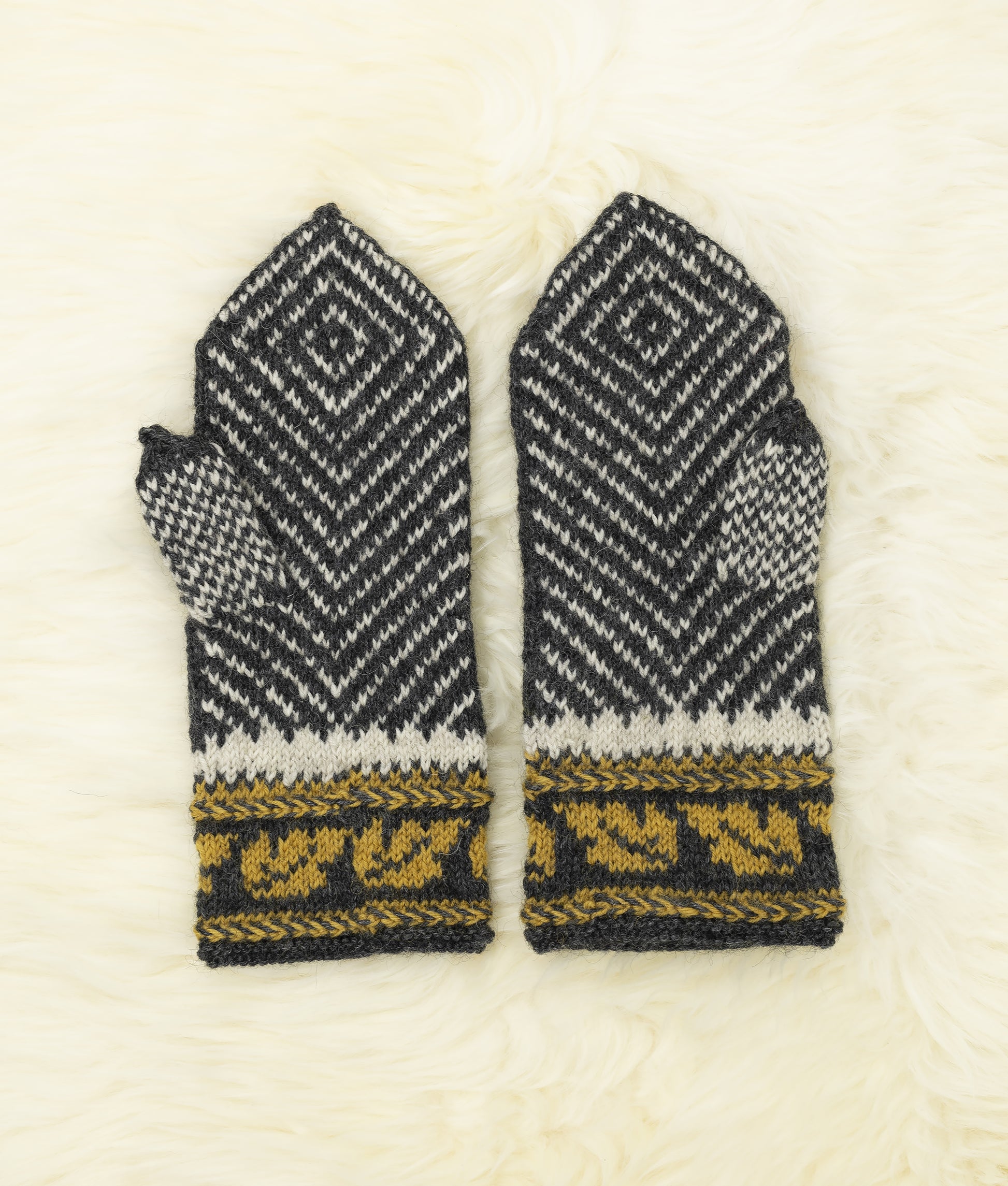 Palms and thumbs of a pair of black, white and yellow hand-knitted mittens with traditional Estonian pattern on a white fur background