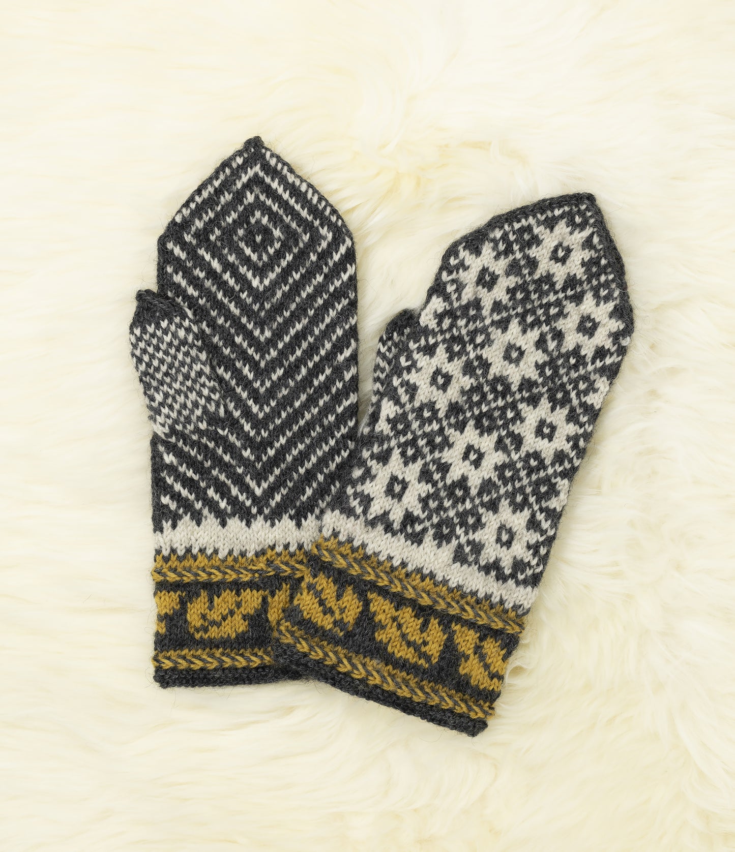 Front and back view of a pair of black, white and yellow hand-knitted mittens with traditional Estonian pattern on a white fur background