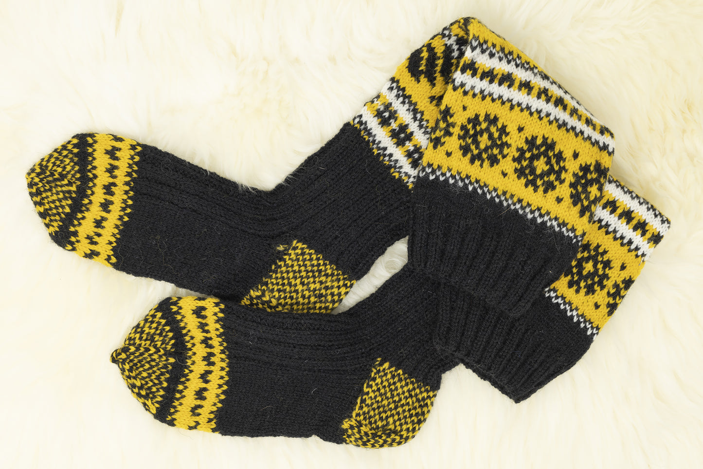 Pair of black, yellow and white hand-knitted Estonian socks on a white background