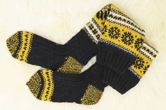 Pair of black, yellow and white hand-knitted Estonian socks on a white background