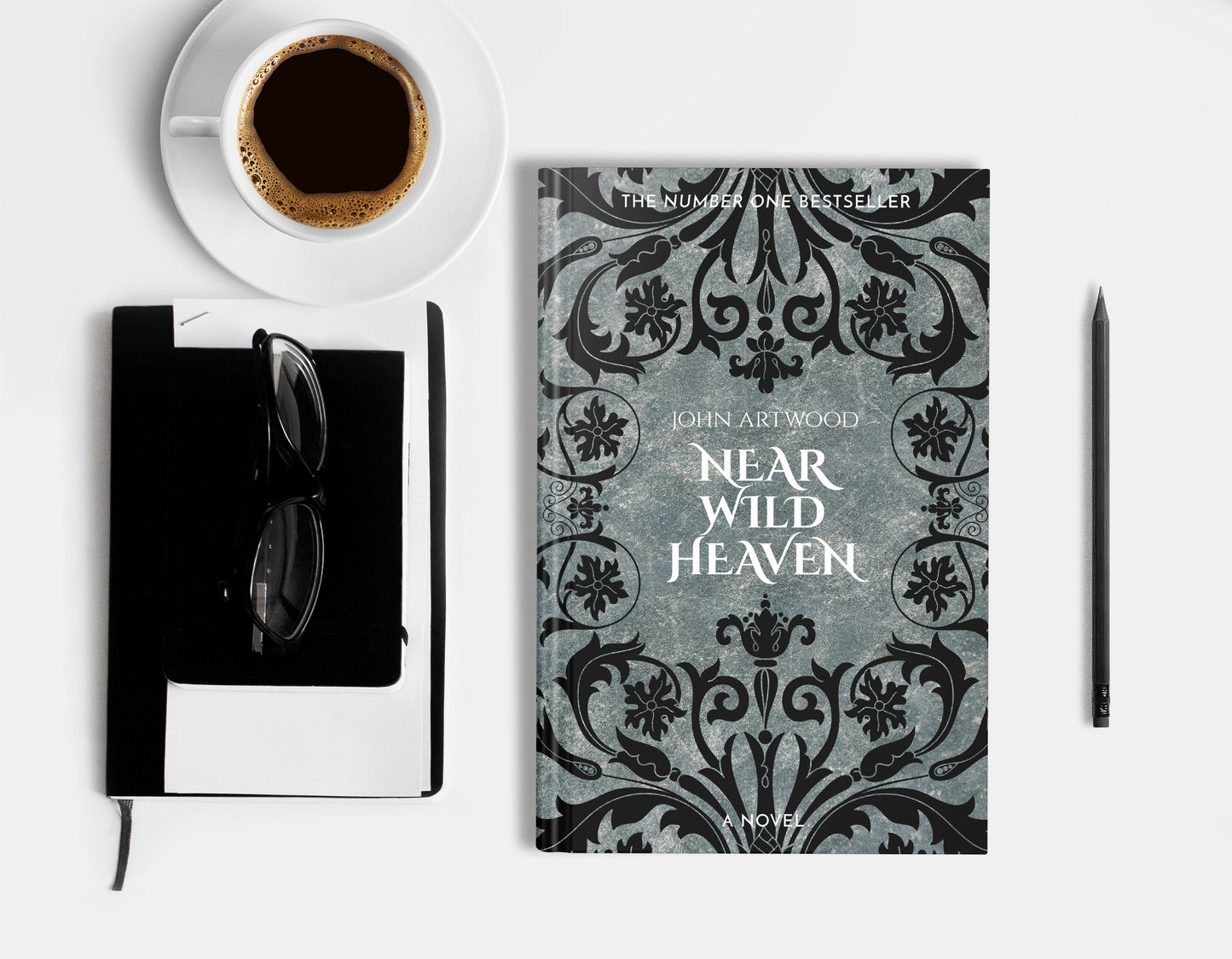 A hardcover book featuring black baroque ornament on a silver background, displaying on a white surface with cup of coffee, a pencil, a notebook and glasses