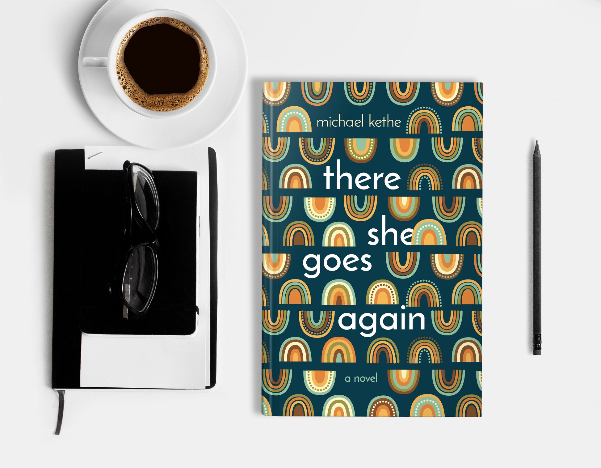 A hardcover book featuring colorful rainbow ornament of a dark teal background, displaying on a white surface with cup of coffee, a pencil, a notebook and glasses