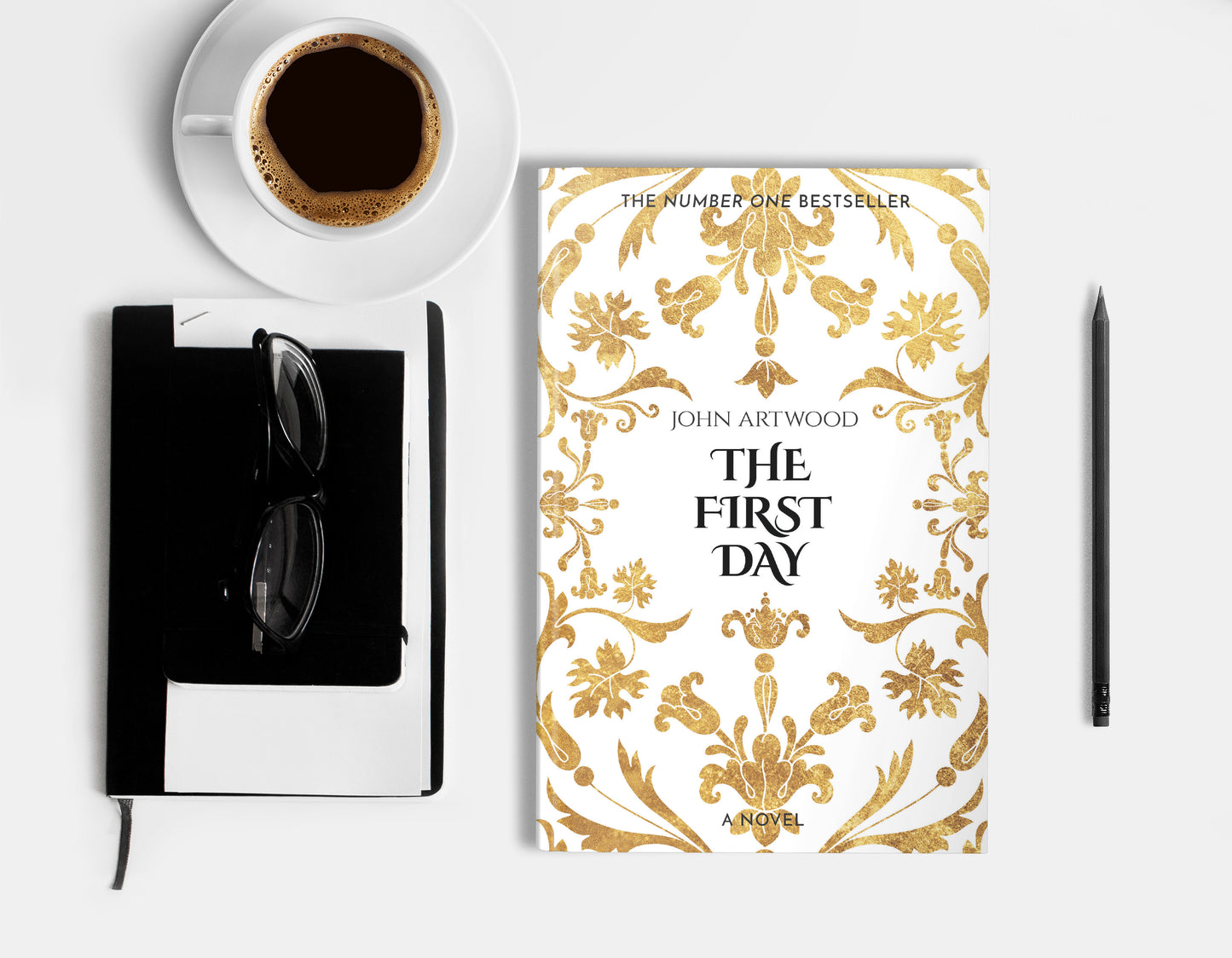 A hardcover book featuring gold baroque ornament on a white background, displaying on a white surface with cup of coffee, a pencil, a notebook and glasses