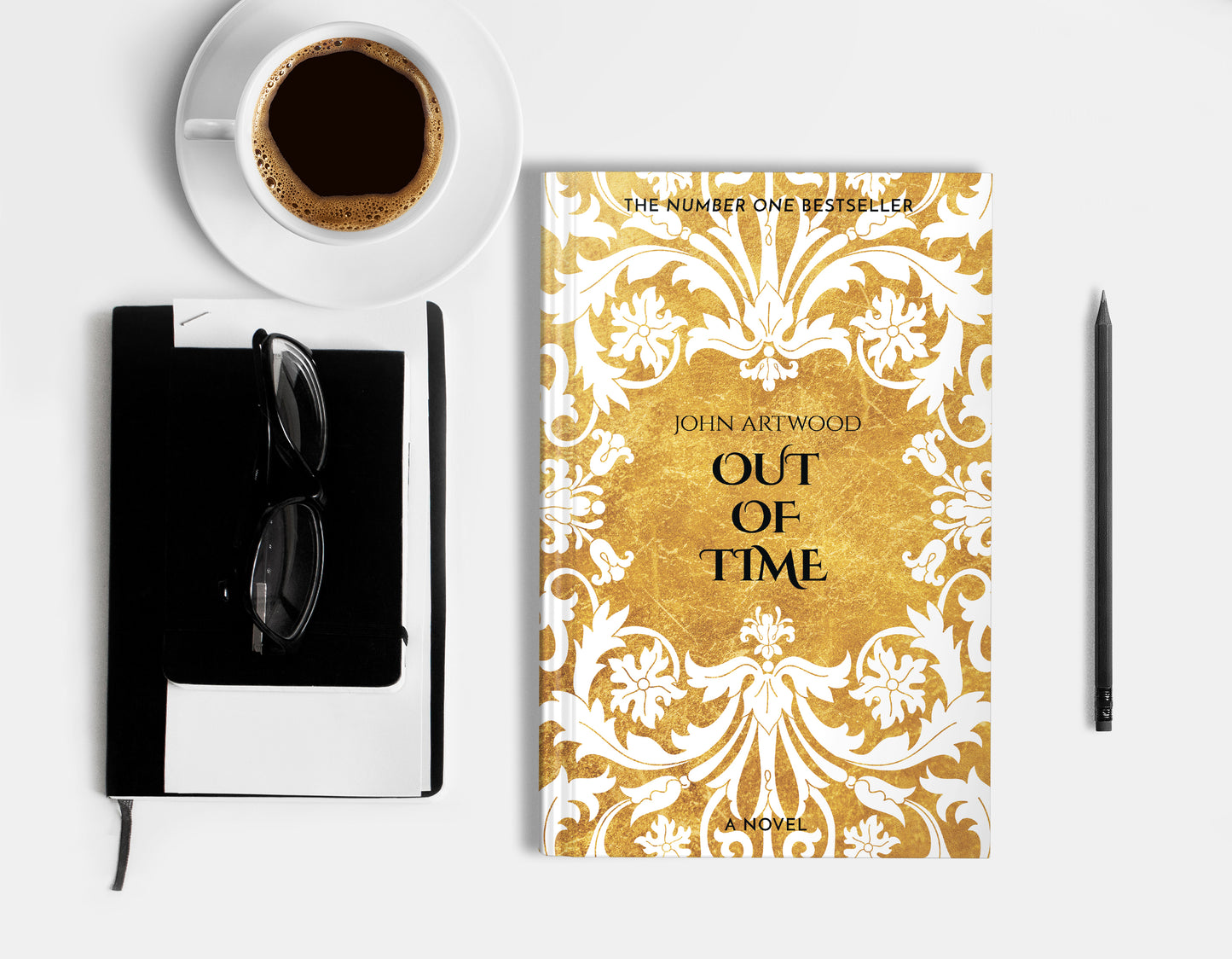 A hardcover book featuring white baroque ornament on a gold background, displaying on a white surface with cup of coffee, a pencil, a notebook and glasses