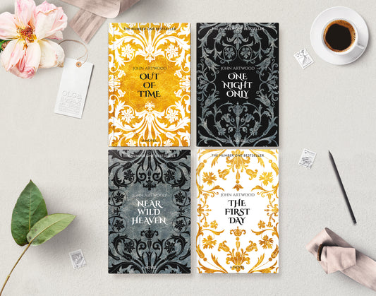 Four book series covers with baroque ornaments in gold, black, silver and white, layng flat on a gray surface accompanied with a cup of coffee