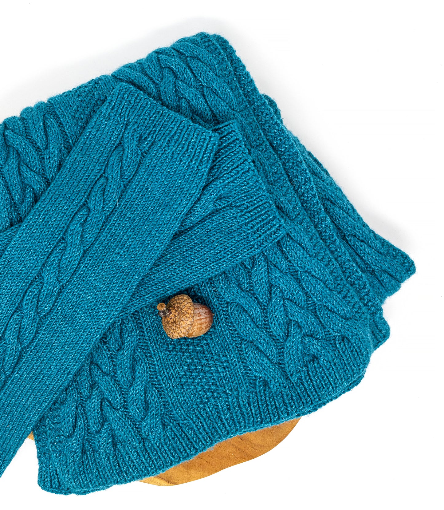 Details of a pair of cable-knit fingerless gloves and matching scarf in teal merino wool on a white background