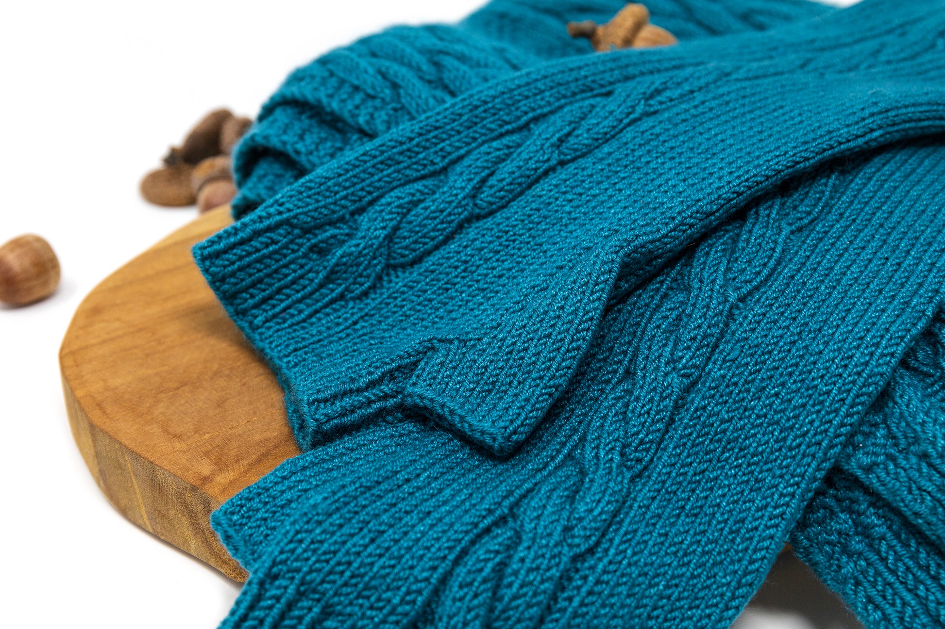 Close-up of a pair of cable-knit fingerless gloves and matching scarf in teal merino wool