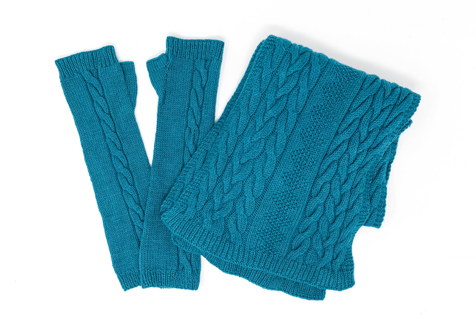 A pair of cable-knit fingerless gloves and matching scarf in teal merino wool laid flat on a white background