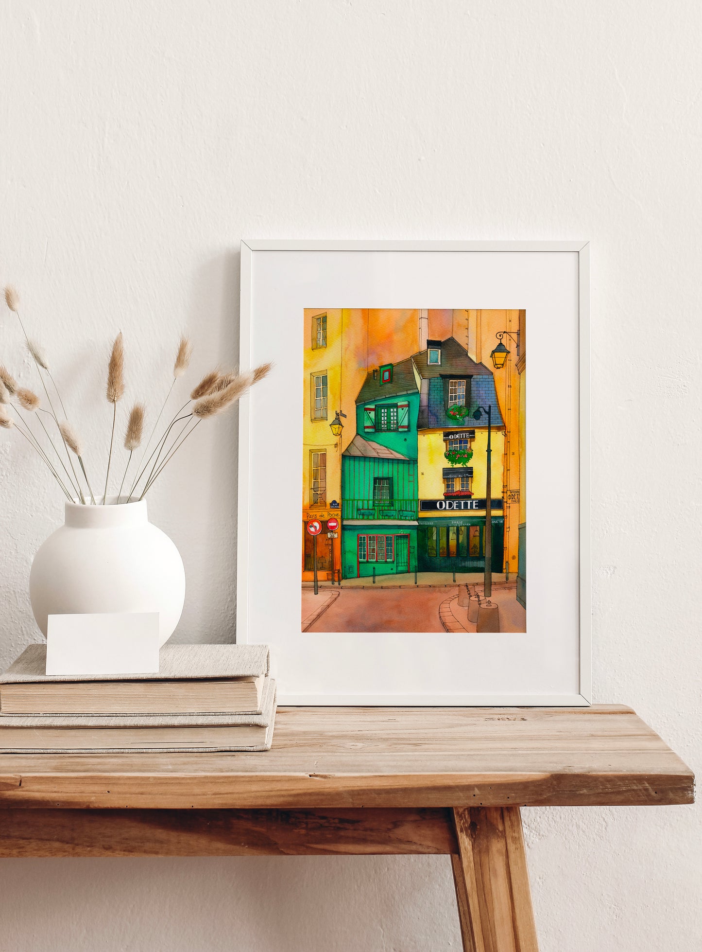 Café Odette in Paris watercolor and ink artwork, displayed in a white frame on a wooden table