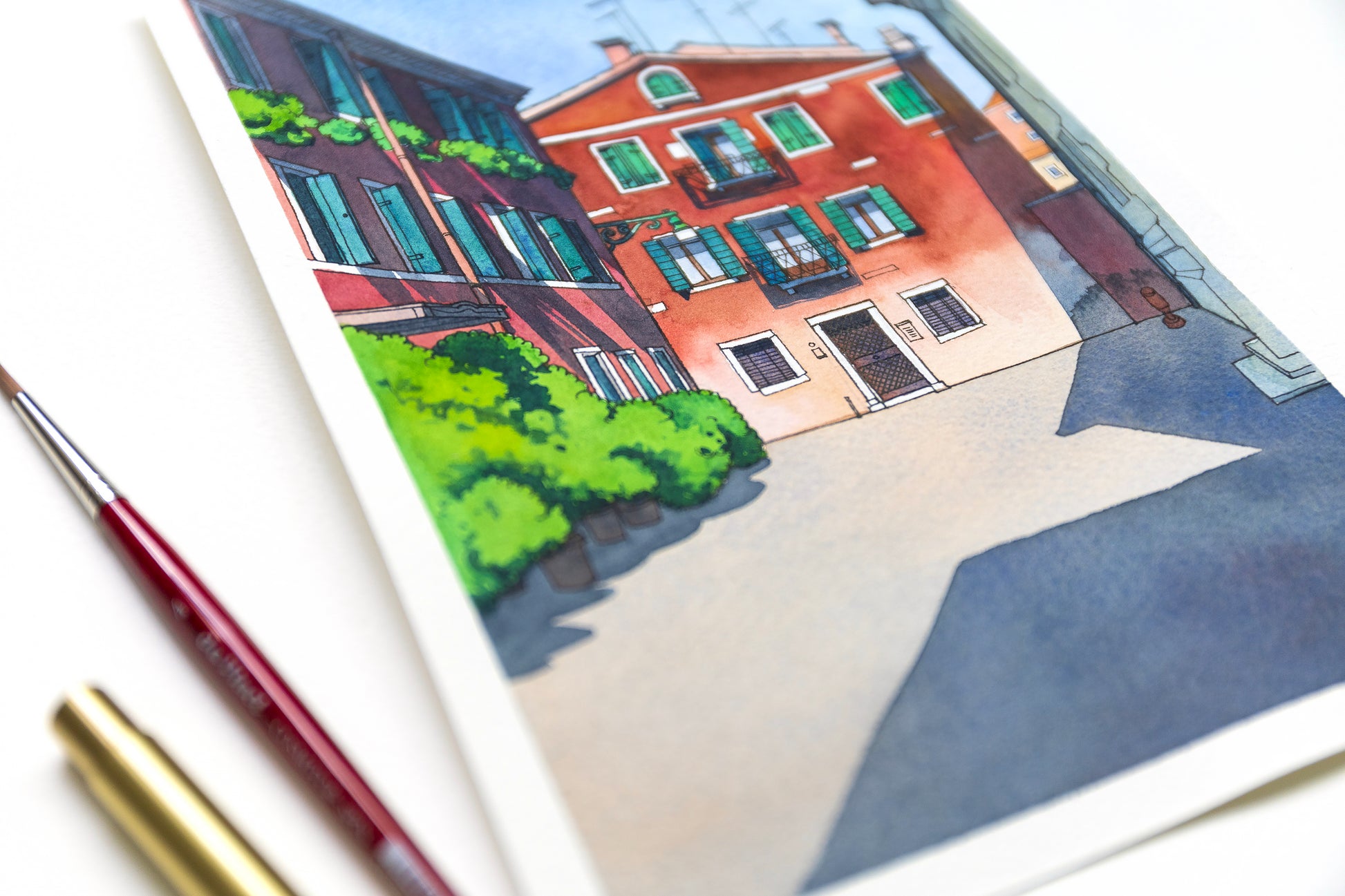 Close up of original watercolor and ink  illustration of Calle Sechera in Venice, Italy, accompanied by two paintbrushes.