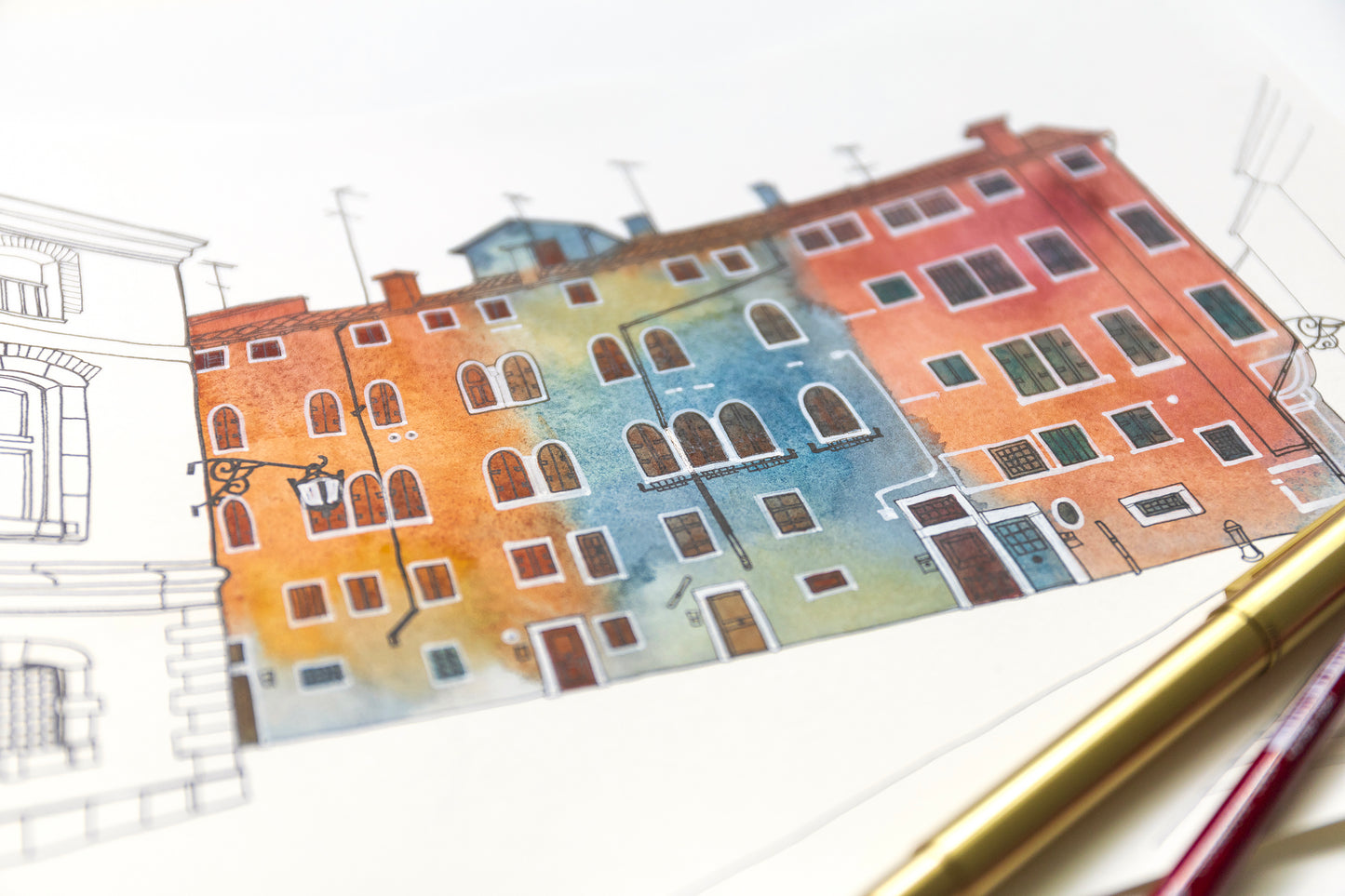 Close-up of a watercolor and ink painting of Venetian Campo San Geremia on a white surface with a pen and paintbrush