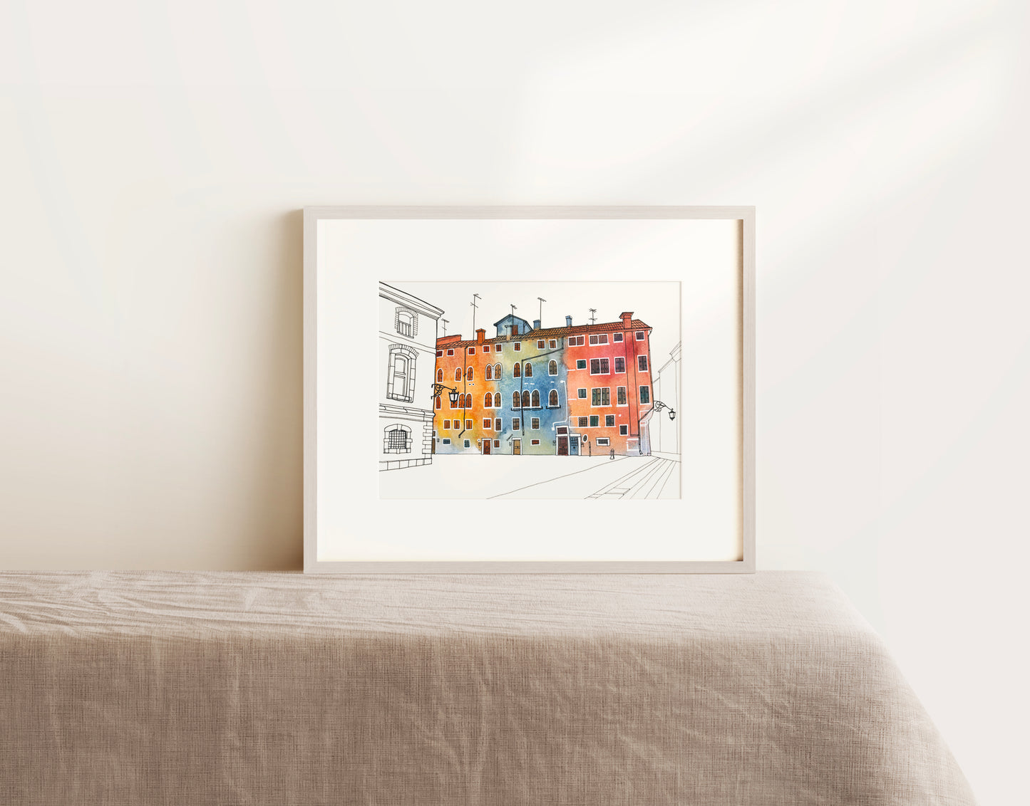 Framed watercolor and ink artwork of colorful Venetian Campo San Geremia on a white wall on a table.