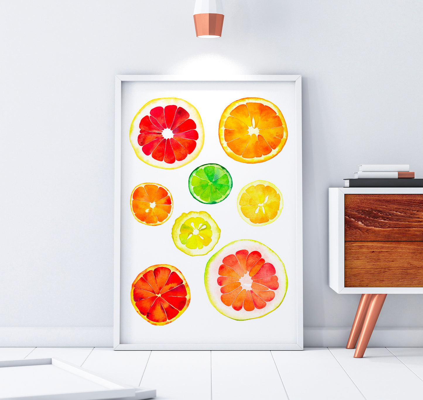 A framed watercolor art print featuring colorful citrus slices chart, including grapefruit, orange, lime, and lemon, displayed on a white wall next to a wooden side table.