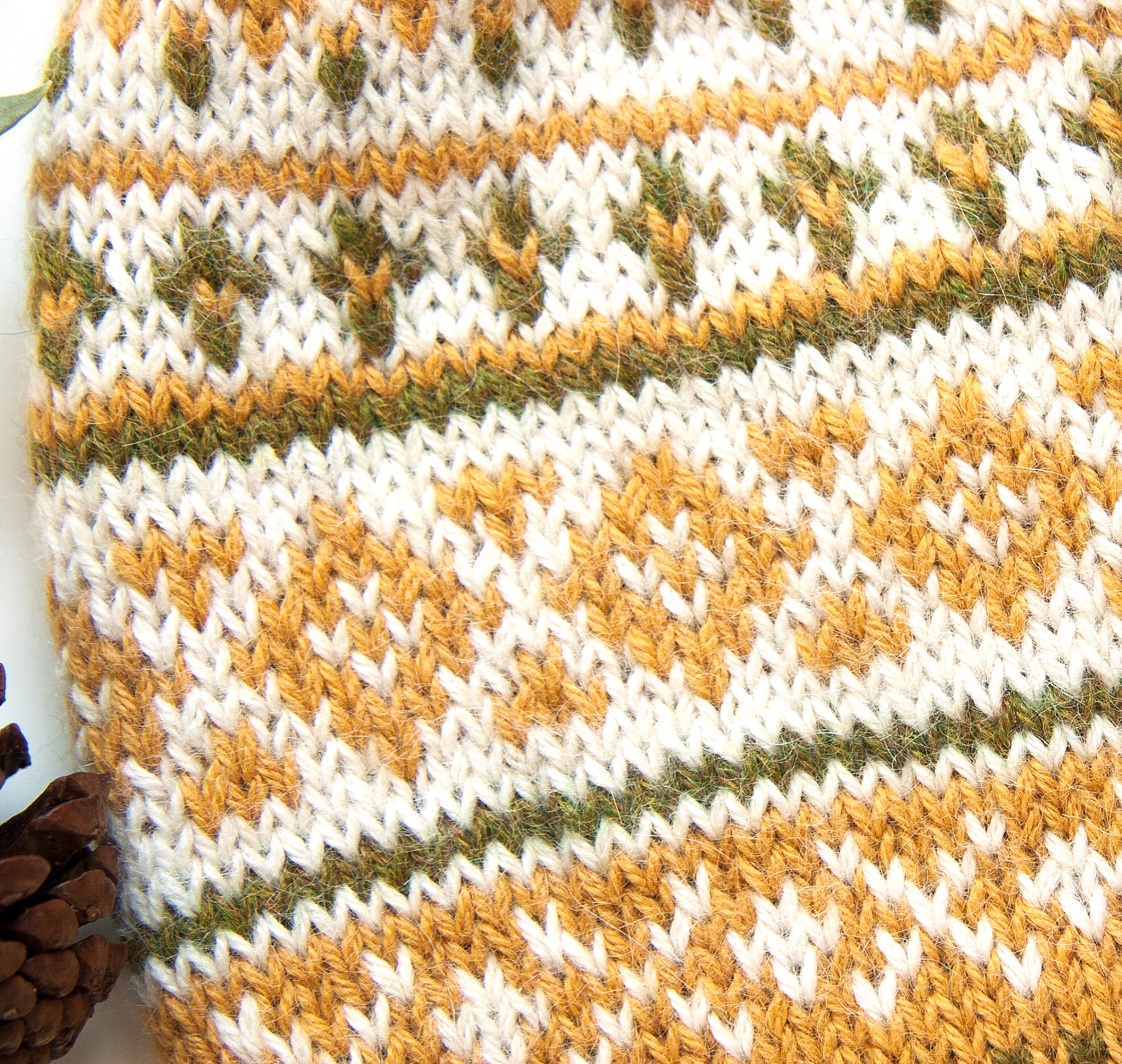 A close-up of a Fair Isle hand-knitted alpaca hat in yellow, white, and green.