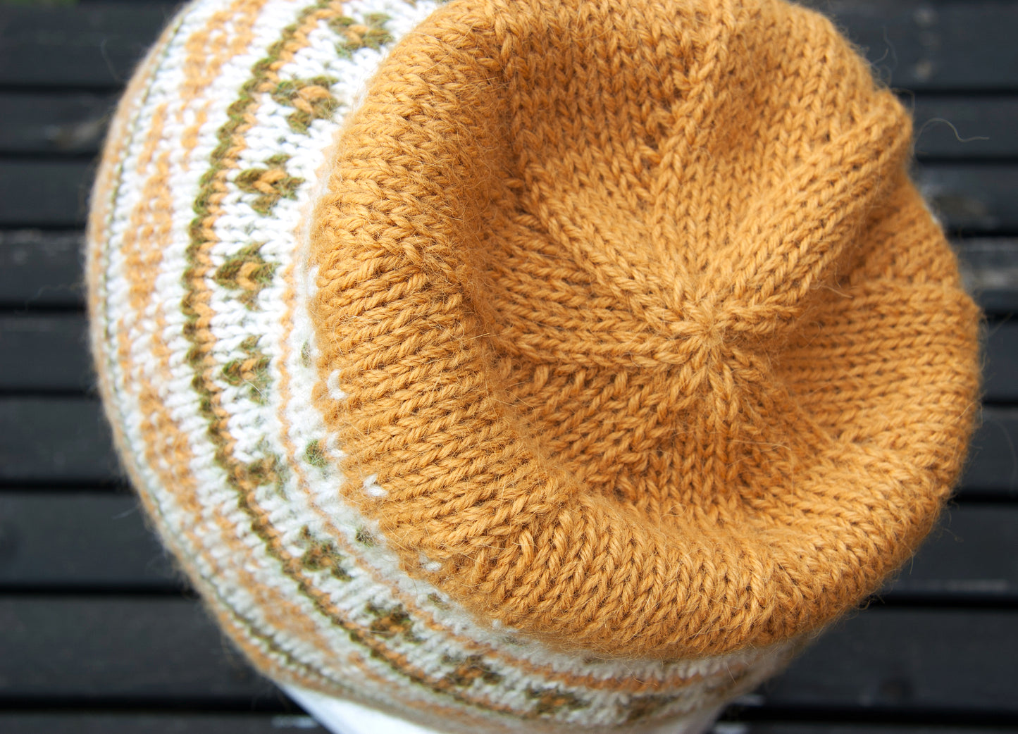 A close-up of a hand-knitted alpaca beanie hat, showing a yellow crown with a white and olive green floral pattern band.