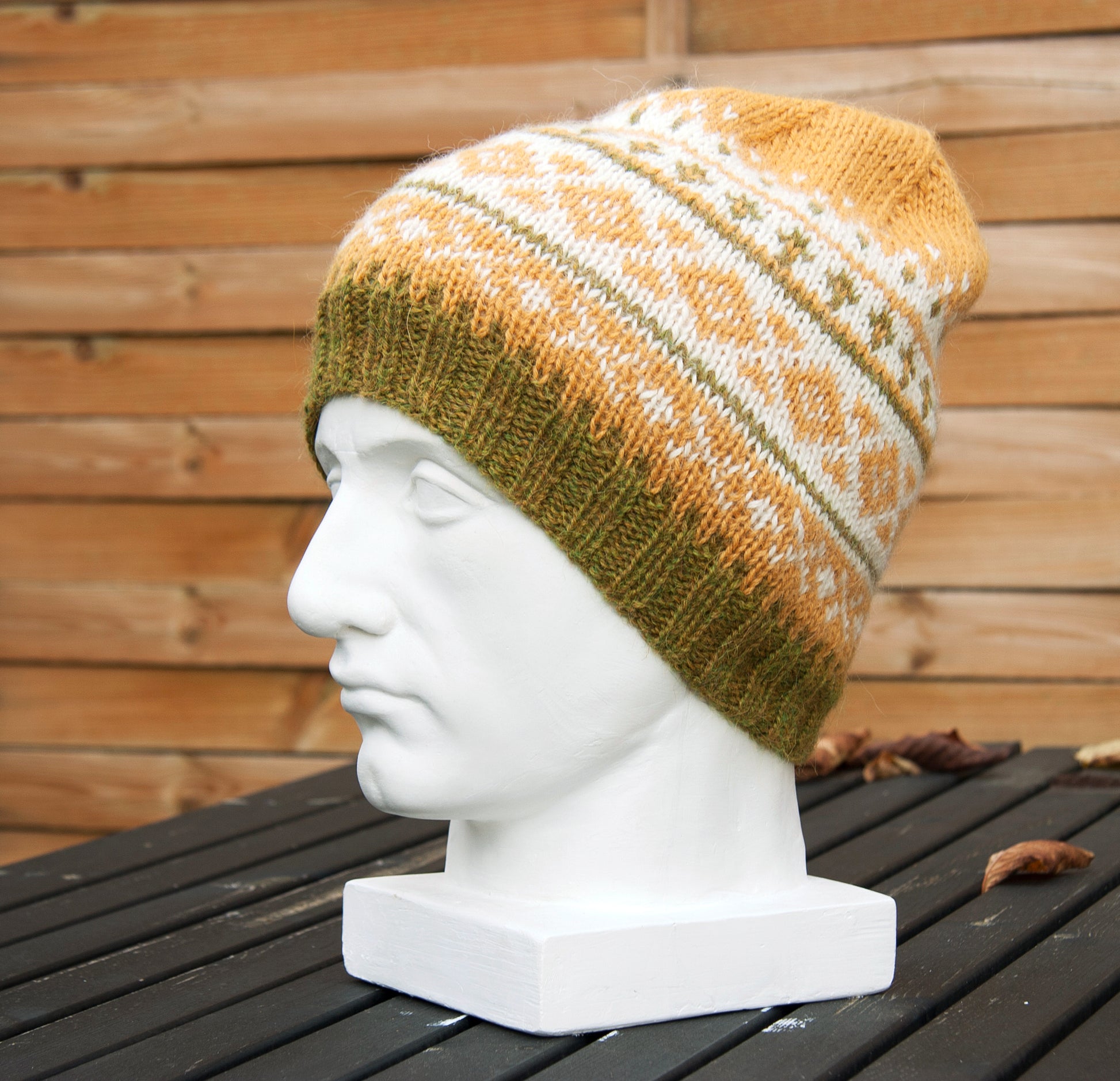 Fair Isle hand-knitted alpaca hat in yellow, white, and green displayed on a white plaster bust