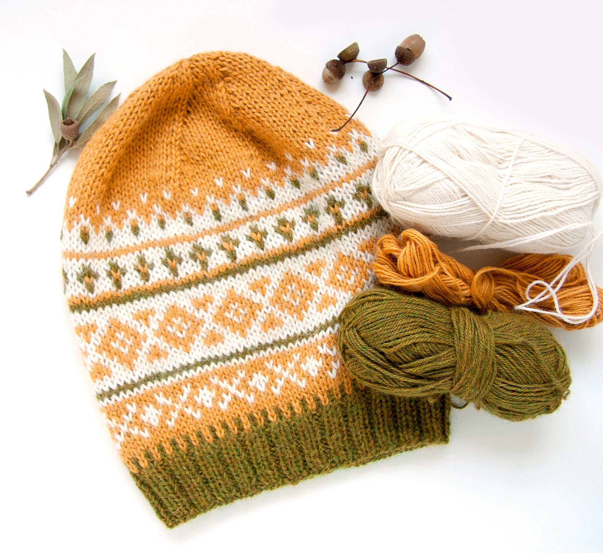 Fair Isle hand-knitted alpaca hat in yellow, white, and green displayed with yarn balls