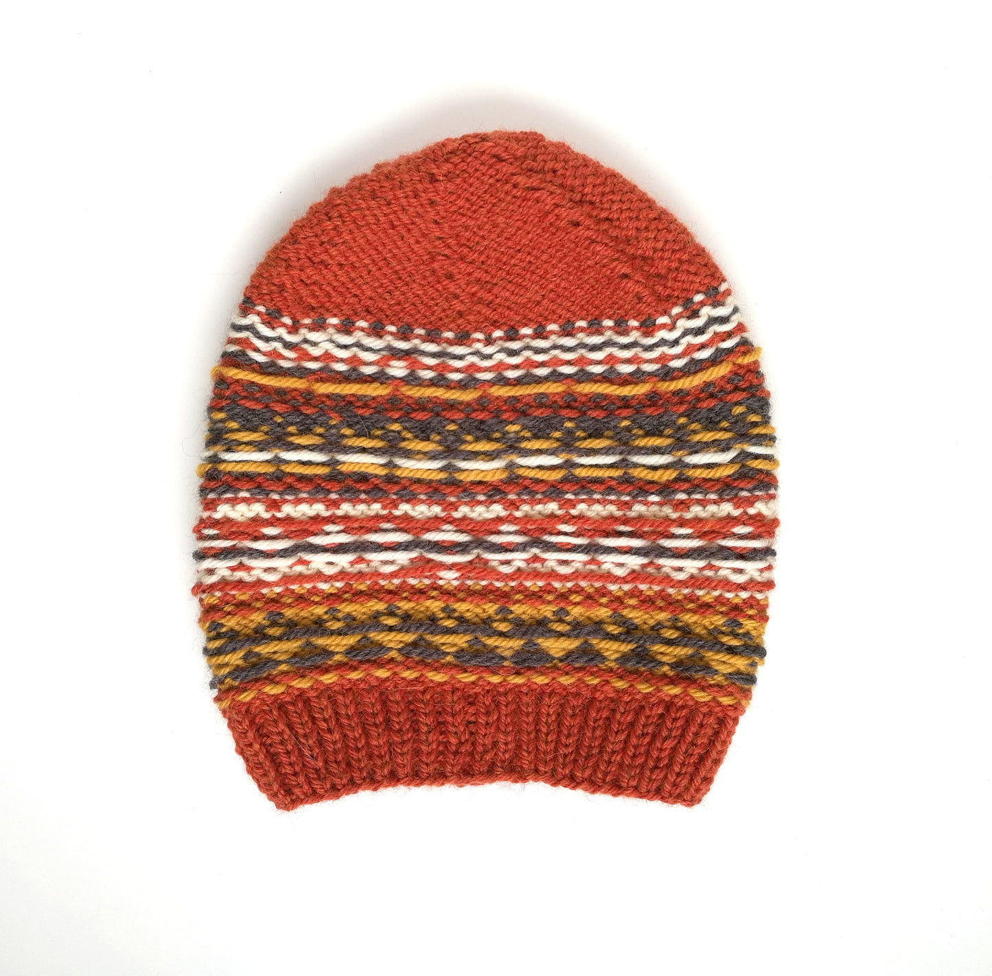 A hand-knitted Fair Isle style hat made of wool and alpaca yarn, with an orange and multicolored geometric pattern, displayed inside out