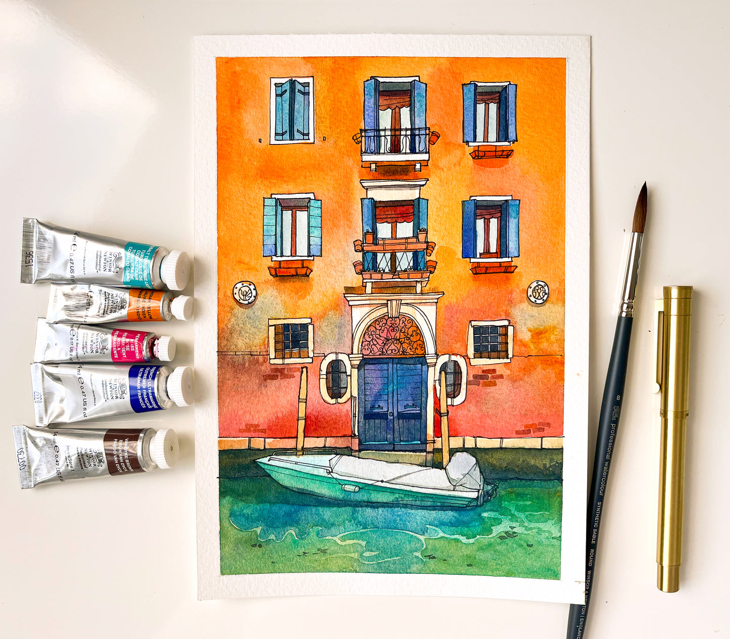 Original watercolor painting of a yellow house with a boat on Fondamenta de la Misericordia in Venice, accompanied by art supplies