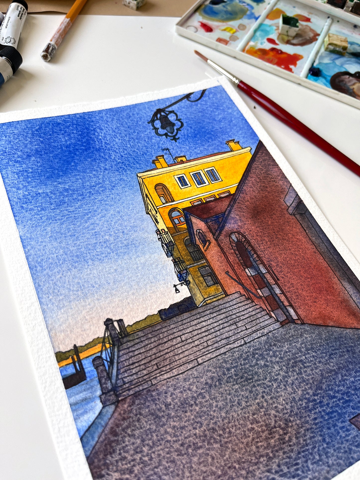 Original watercolor and ink artwork of a yellow building on Fondamenta Santa Giustina in Venice, Italy, accompanied by art supplies