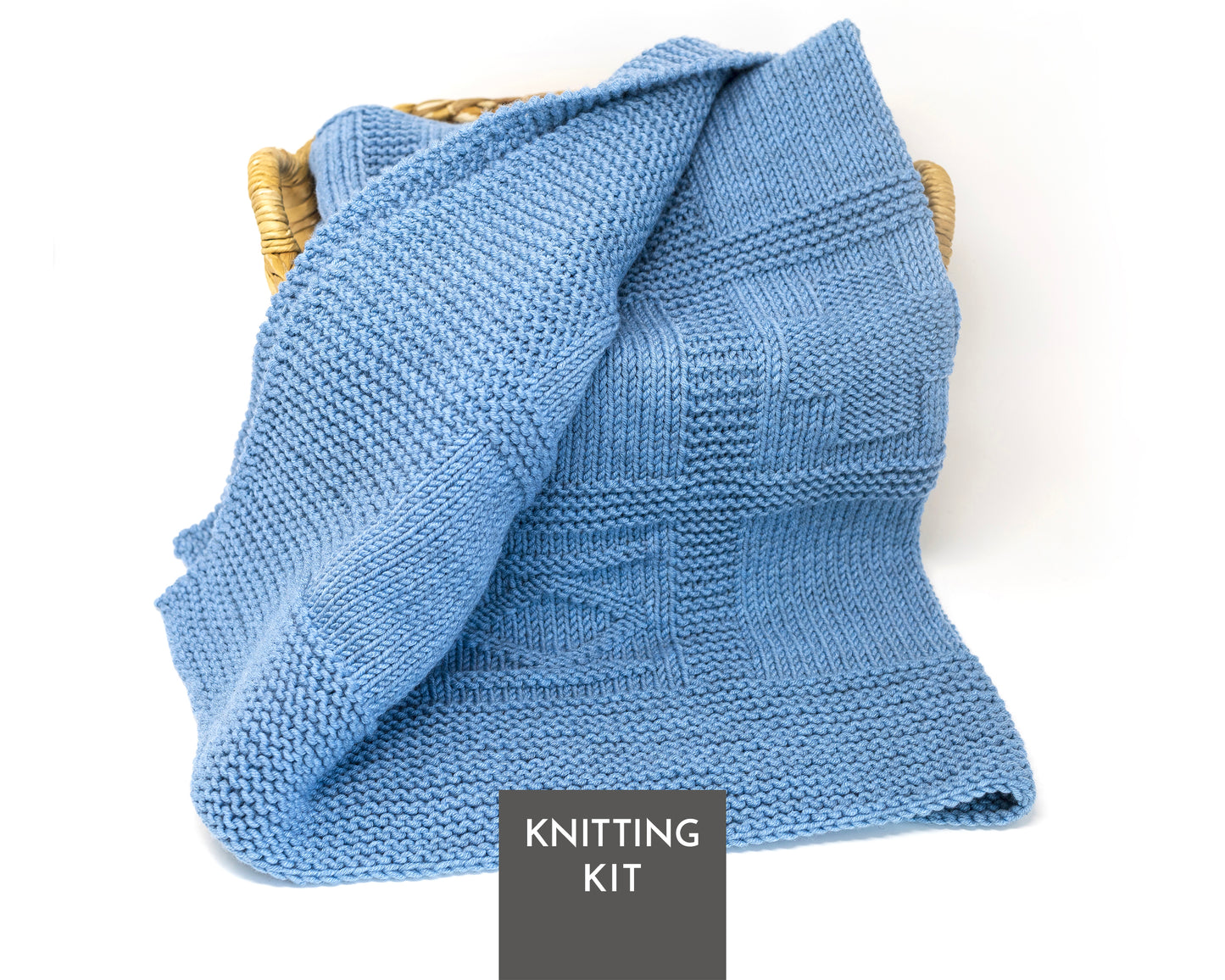 A light blue geometric knitted blanket draped over a woven basket, with a dark gray label at the bottom reading 'KNITTING KIT'.