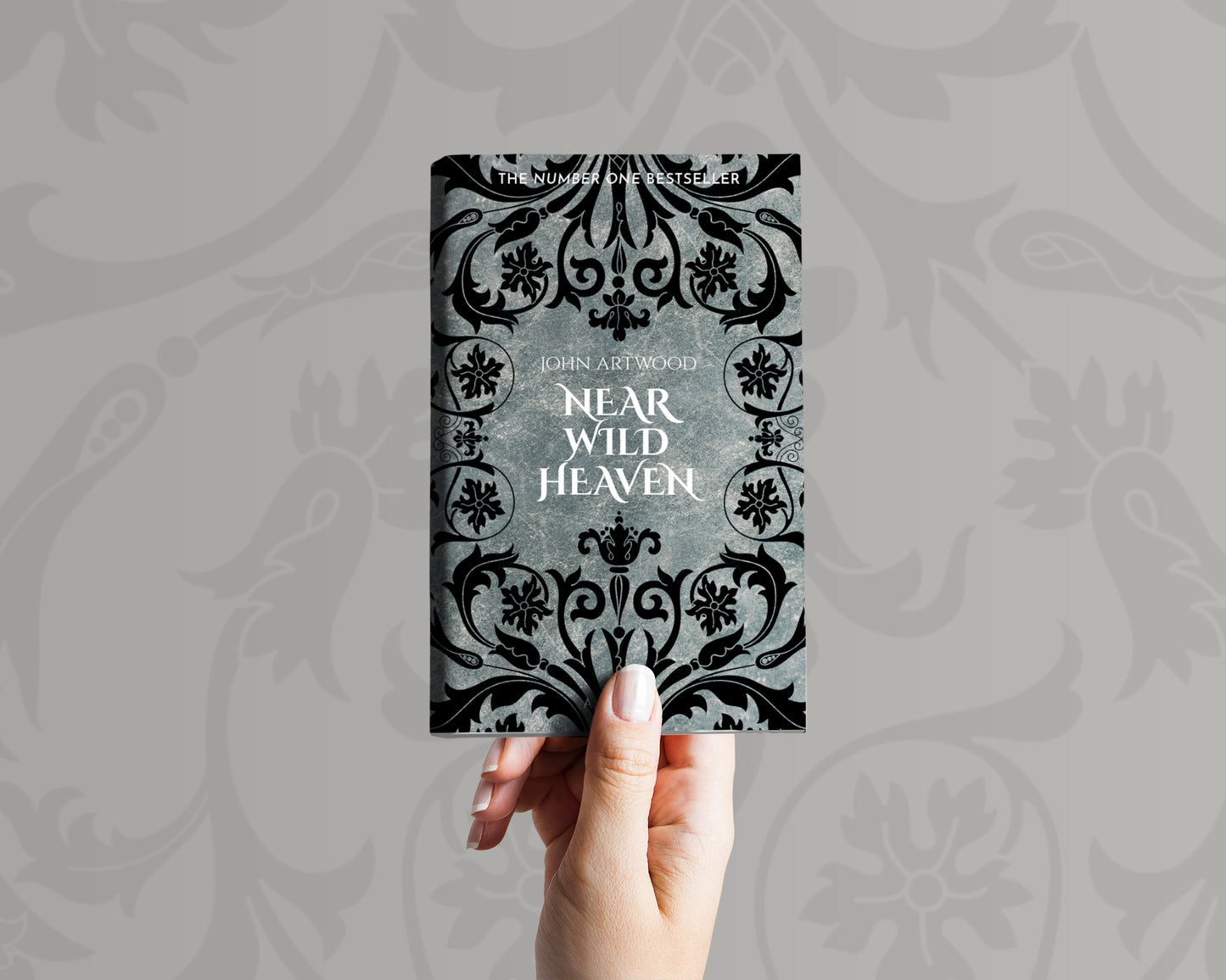 A hand holds a book with black baroque ornament on a silver background on its cover