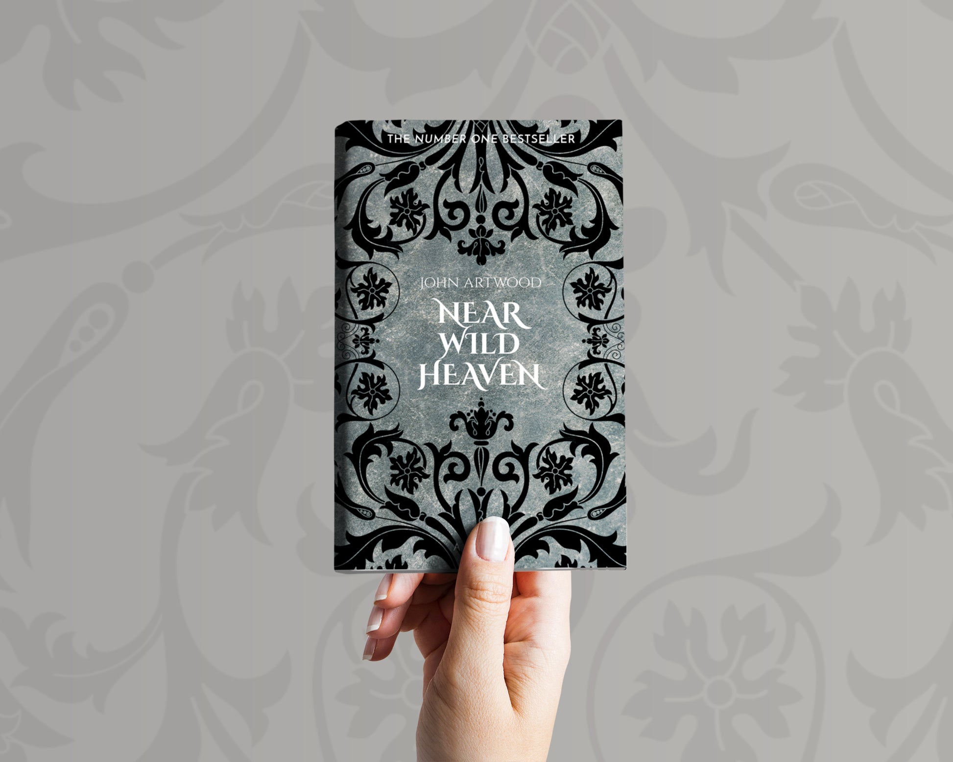 A hand holds a book with black baroque ornament on a silver background on its cover