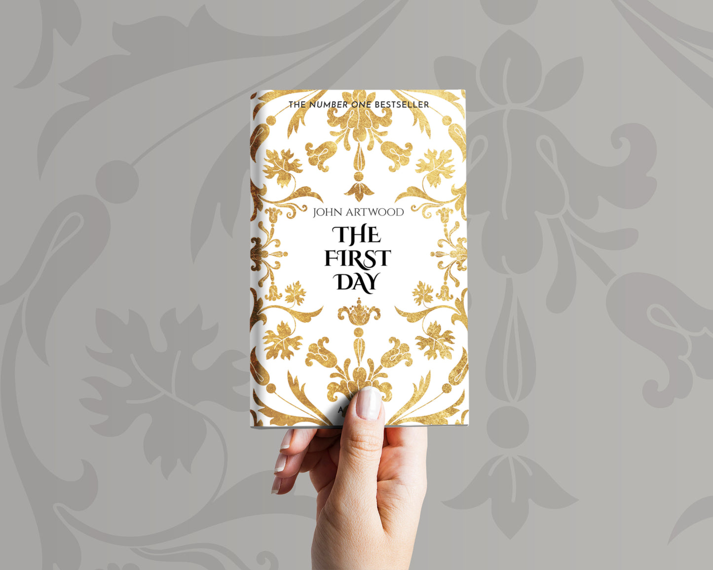 A hand holds a book with a gold baroque ornament on a white background on its cover.