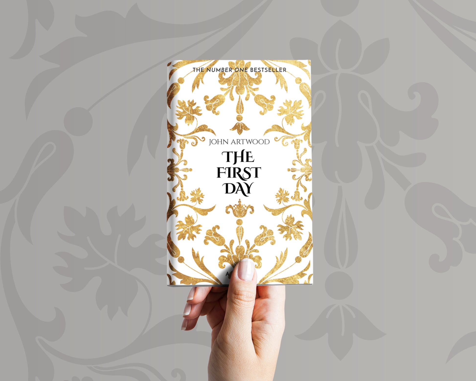 A hand holds a book with a gold baroque ornament on a white background on its cover.