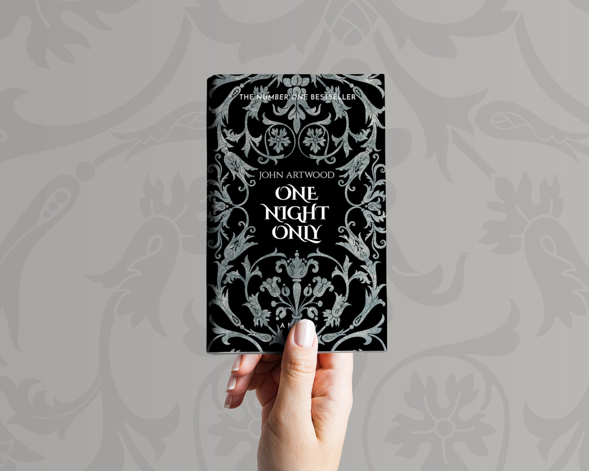 A hand holds a book with silver baroque ornament on a black background on its cover