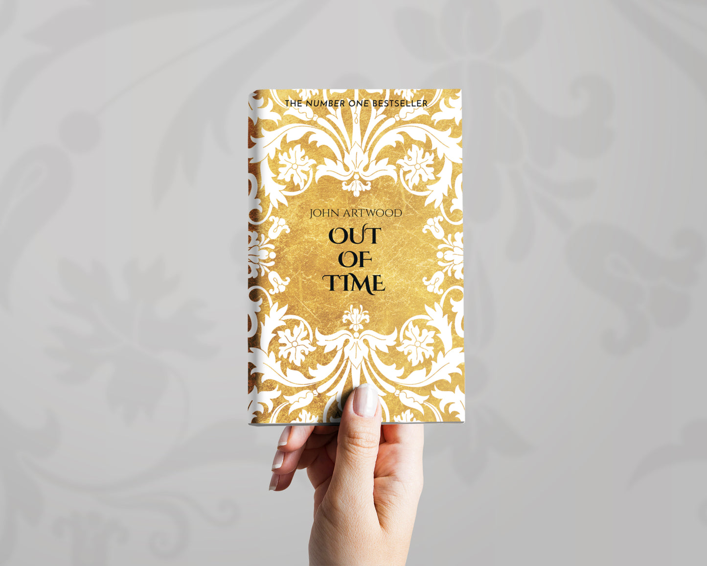 A hand holds a book with white baroque ornament on a gold background on its cover