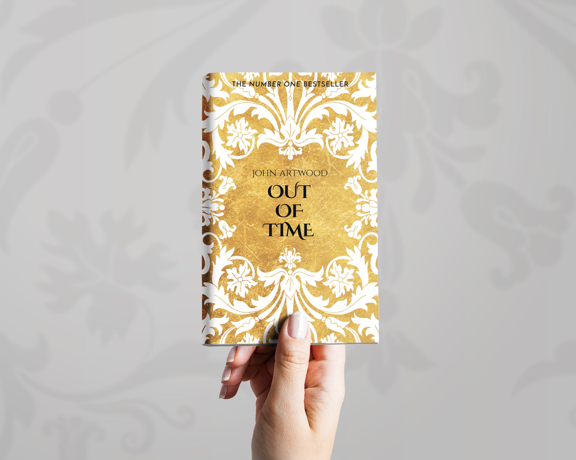 A hand holds a book with white baroque ornament on a gold background on its cover