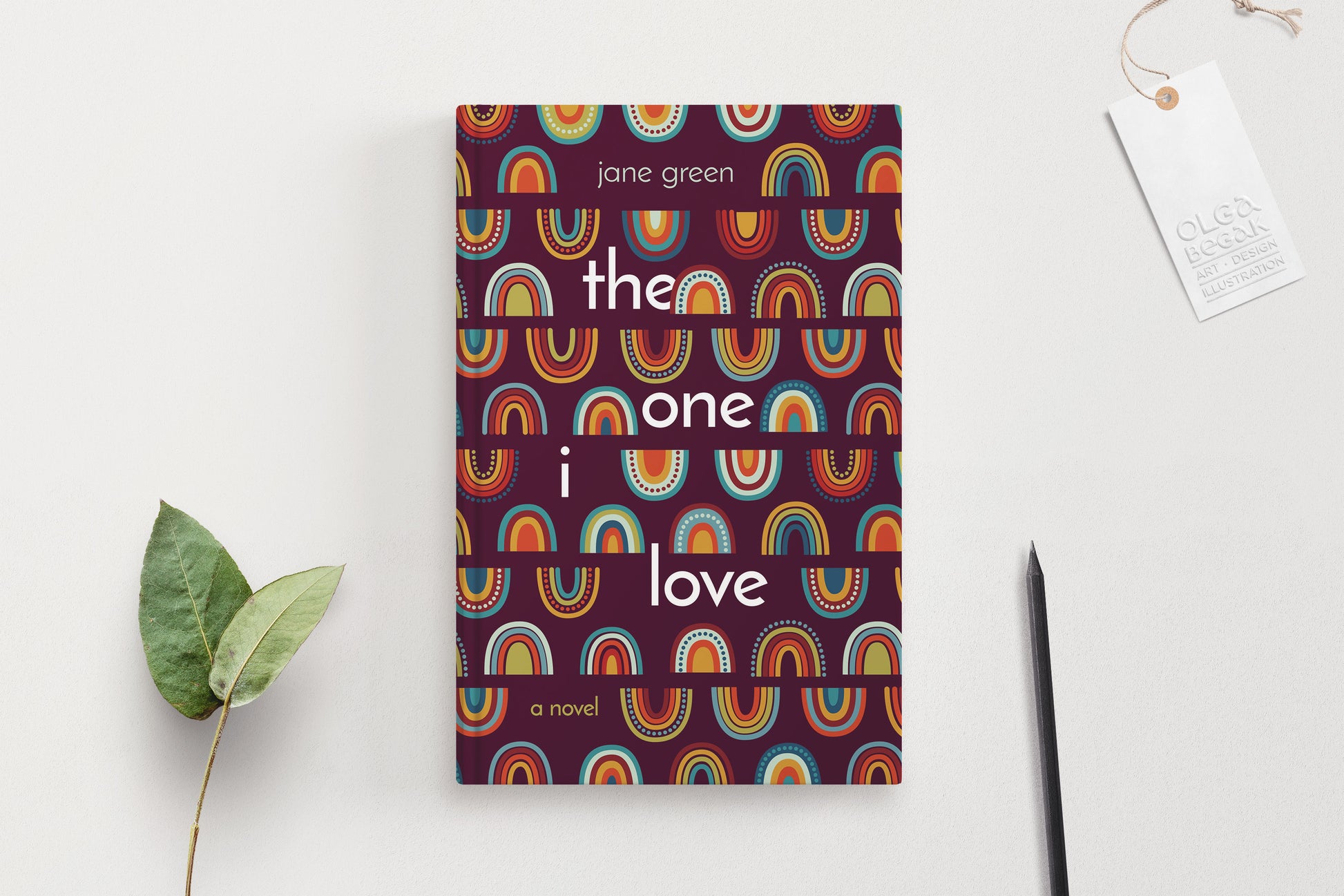 A hardcover book featuring colorful rainbow ornaments on a purple background, displaying on a white surface with pencil and eucalyptus branch.