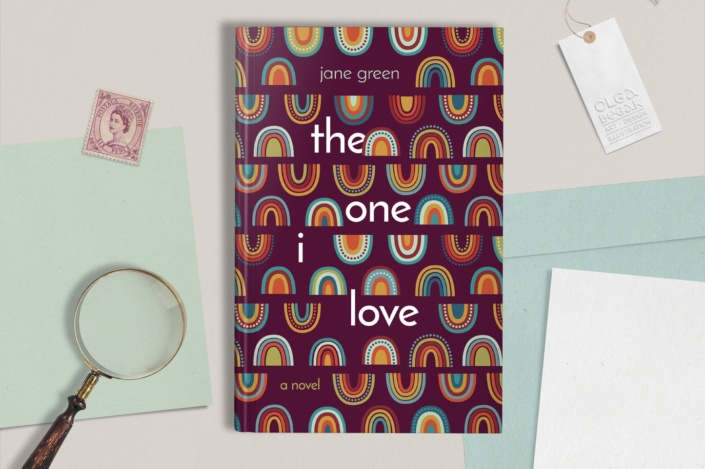 A hardcover book featuring colorful rainbow ornaments on a purple background, displaying on a light gray surface with paper sheets, magnificent glass and postage stamps.