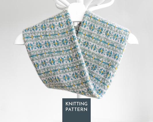 A knitted twisted cowl scarf with a gray, teal blue, and yellow Fair Isle pattern. A dark gray label at the bottom reads 'KNITTING PATTERN'.