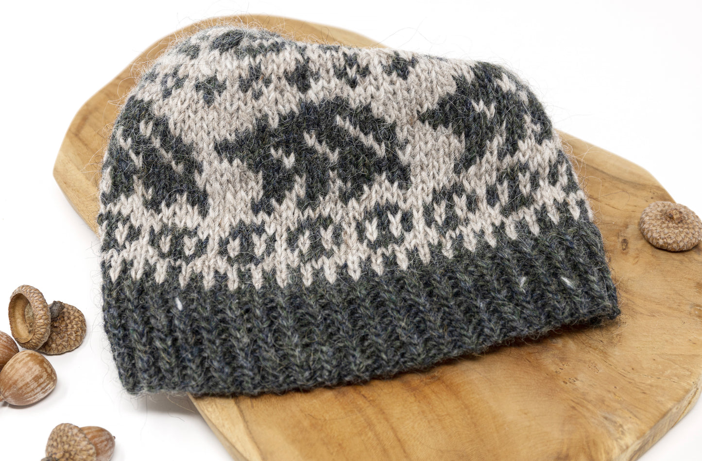 A close-up of a hand-knitted beanie hat with a dark gray-green and light beige Fair Isle style pattern, featuring bears.