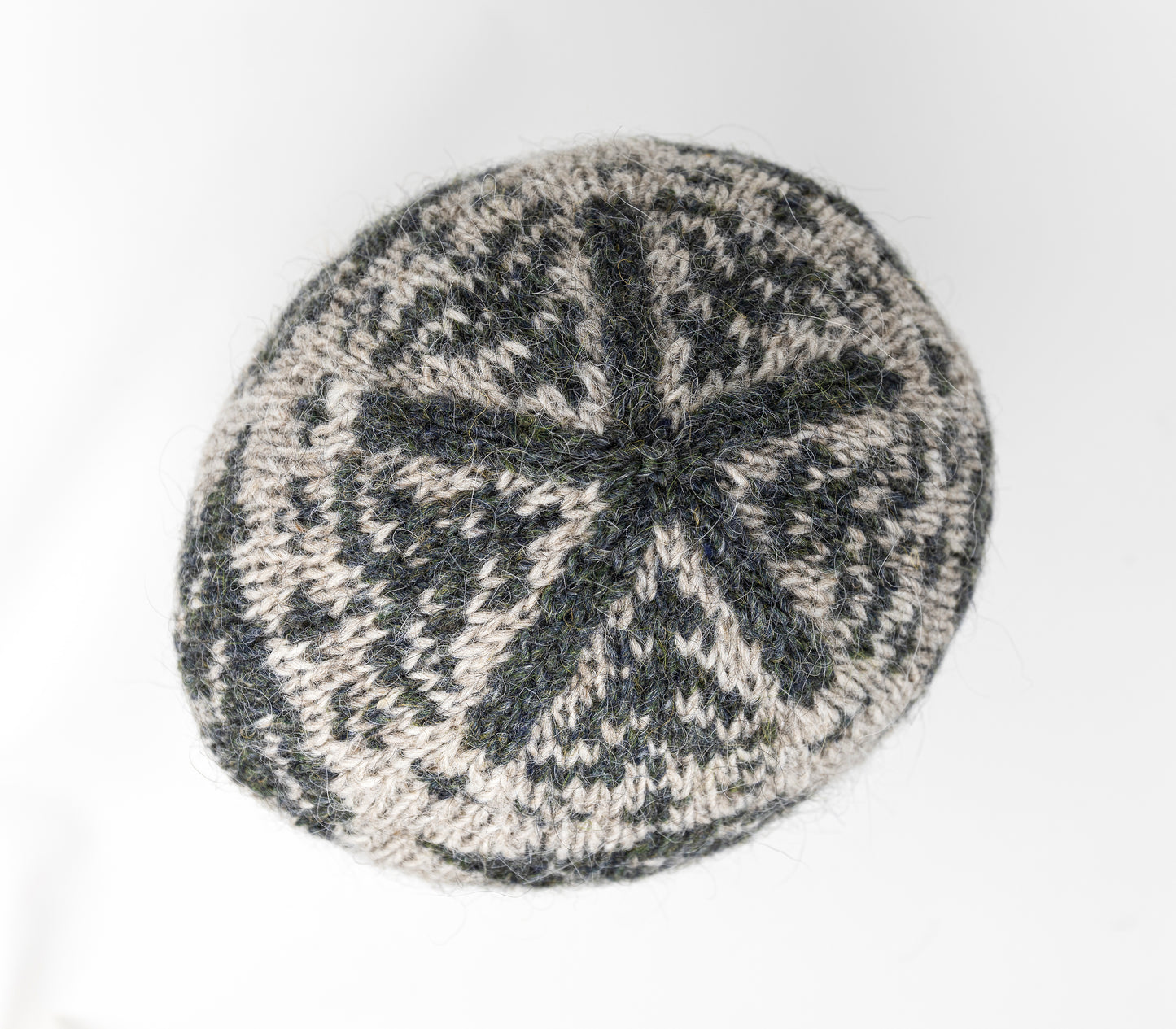 A close-up of a crown of a knitted hat with a dark gray-green and light beige Fair Isle style pattern.