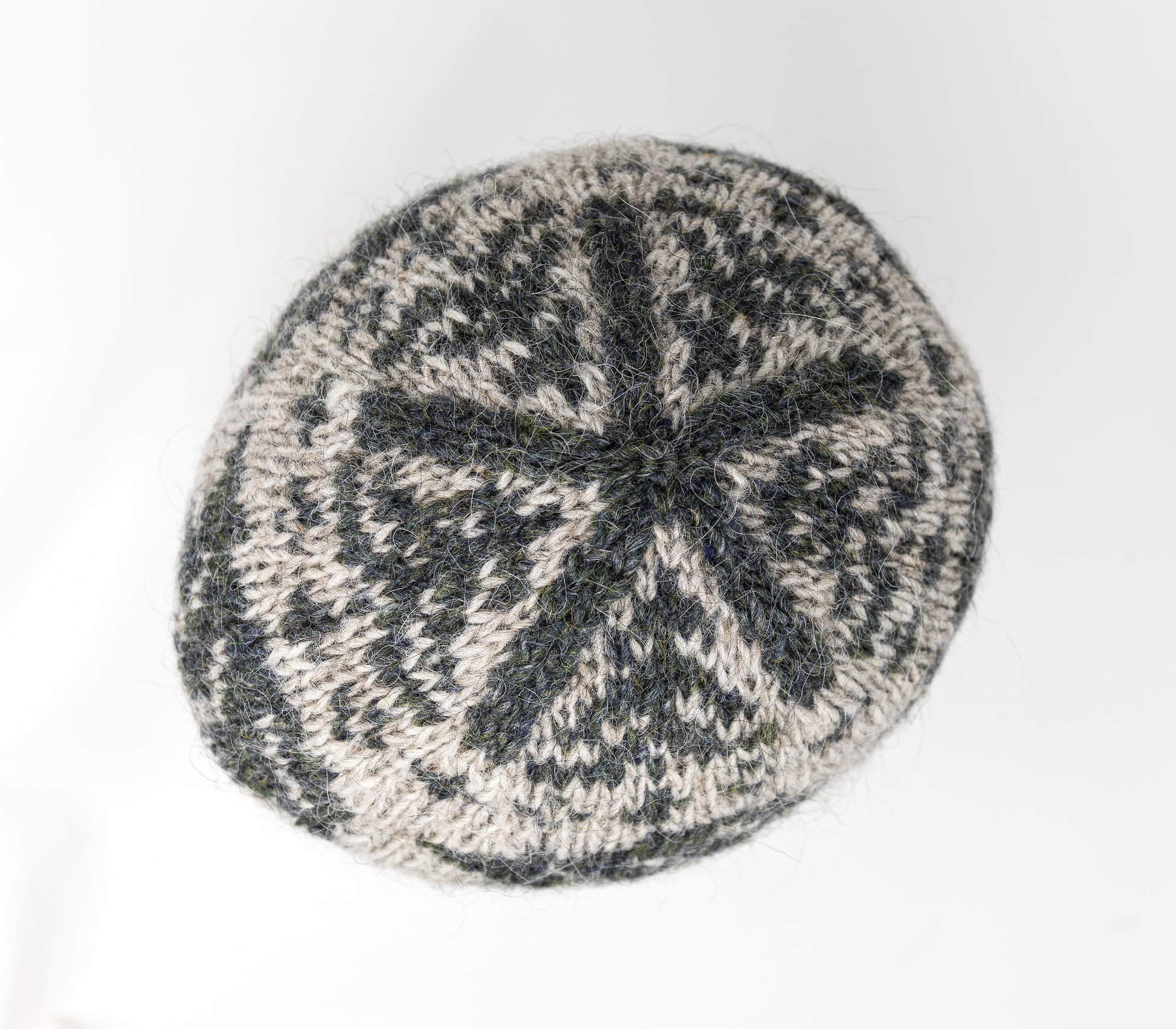 A close-up of a crown of a knitted hat with a dark gray-green and light beige Fair Isle style pattern.