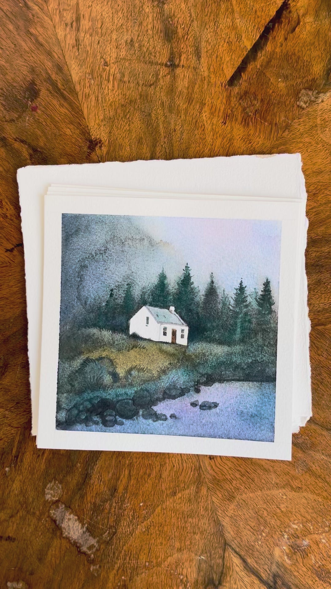 Four watercolor paintings featuring Scottish Highlands — Glencoe, the Pink House at Loch Glass (Culzie Lodge), Allt Dearg cottage on the Isle of Skye, and a remote stone croft near Applecross, displayed on a wooden background